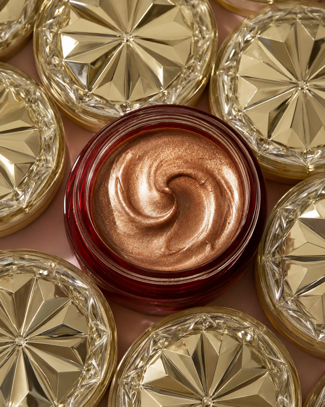 SEVĒNNE Radiance Veil illuminating tallow balm. Open jar of SEVĒNNE Radiance Veil showing swirled champagne-bronze balm
  texture, surrounded by faceted gold lids on a soft pink background