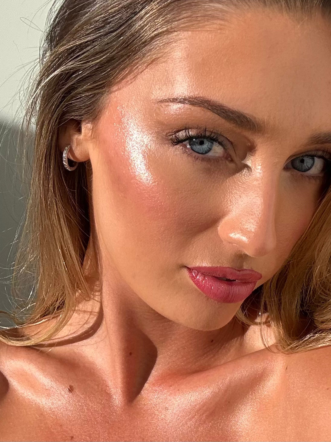 Close-up of a woman with natural makeup and a sun-kissed glow. Radiance Veil on cheekbones and décolletage